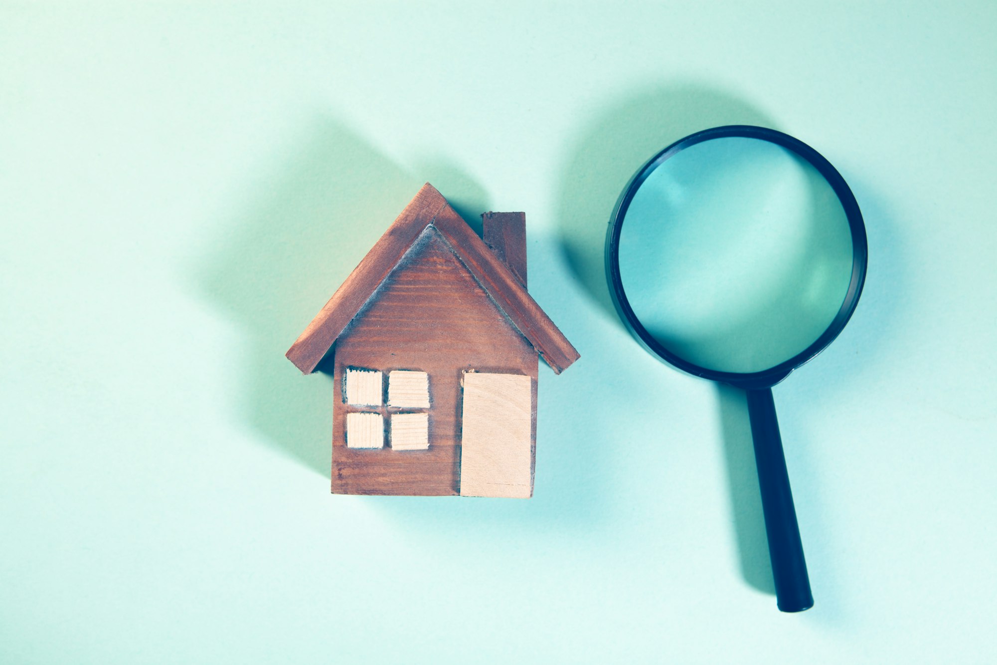Magnifying glass examining a wooden house model, illustrating a thorough home inspection before closing in British Columbia